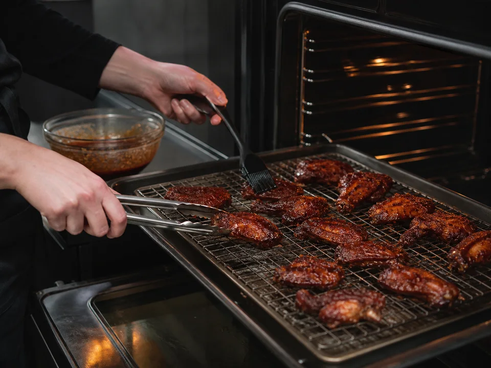 Dunkel glasierte Chicken Wings werden auf einem Rost gewendet und während des Backens dünn bestrichen