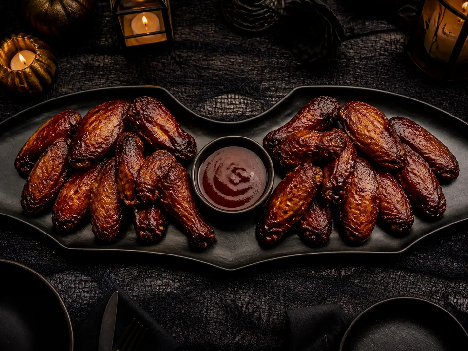 Dunkel glasierte Chicken Wings sind wie zwei Fledermausflügel um eine Schale mit roter Soße angeordnet