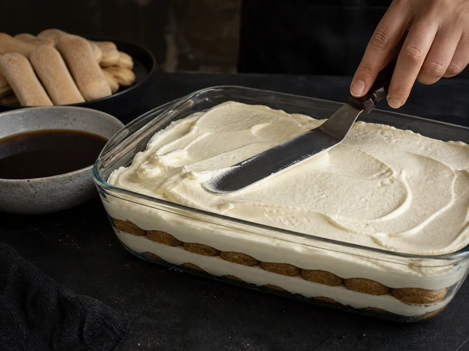 Kaffeegetränkte Löffelbiskuits und Mascarpone-Quark-Creme werden in einer rechteckigen Glasform geschichtet