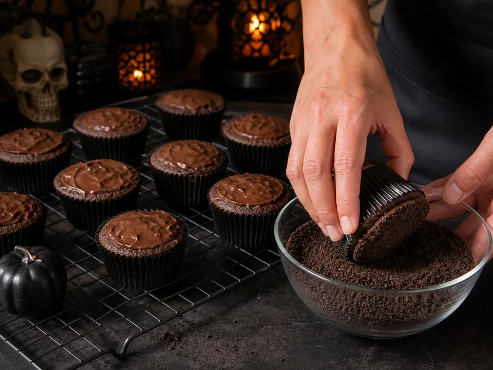 Ausgekühlte Schoko-Muffins werden mit Schokocreme bestrichen und kopfüber in sehr feine dunkle Keksbrösel gedrückt