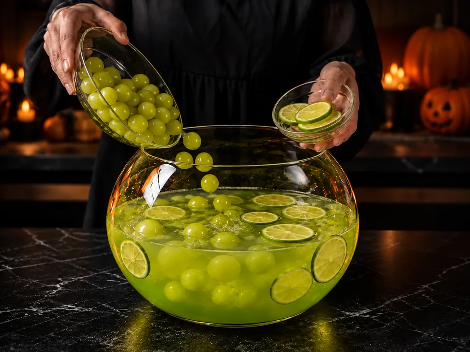 Grüne Trauben und dünne Limettenscheiben werden in die große gläserne Bowleschale mit Apfel-Limetten-Saft gegeben