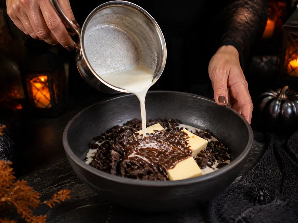 Heiße Sahne wird über fein gehackte dunkle Schokolade und Butter in einer Schüssel gegossen