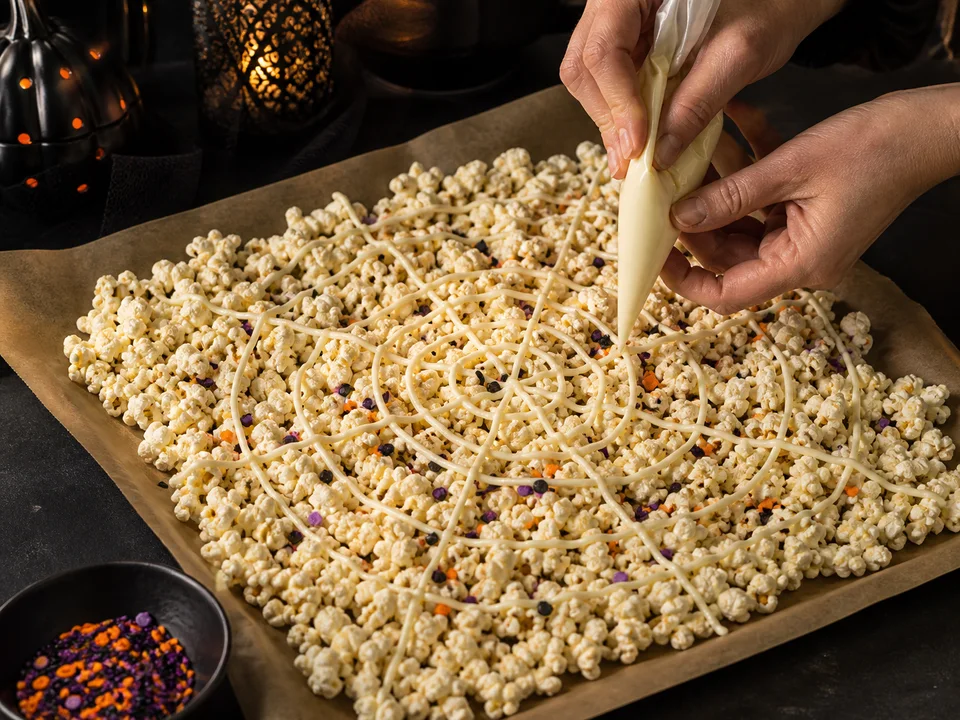 Dünne weiße Schokoladenlinien werden spiralförmig und vom Zentrum nach außen über Popcorn auf Backpapier gezogen